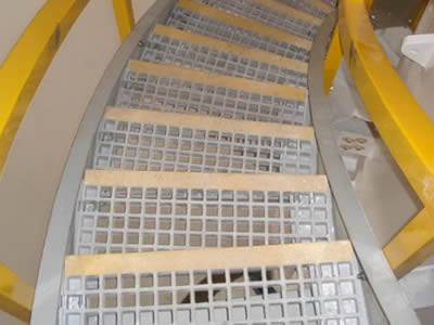 It shows that several stair treads are installed in curved stairs with yellow handrails.